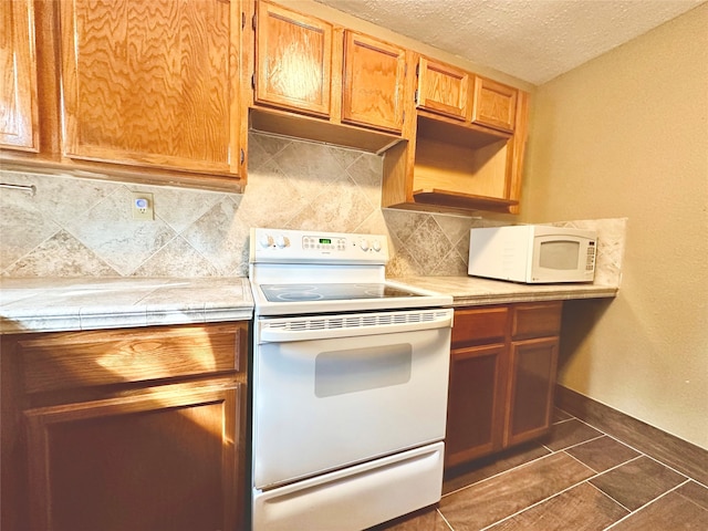 kitchen with a textured ceiling, dark tile patterned flooring, backsplash, and white appliances