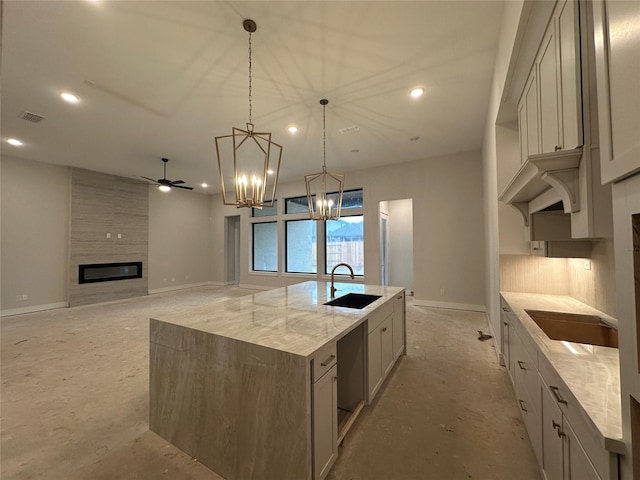 kitchen featuring light stone counters, ceiling fan, a spacious island, sink, and pendant lighting