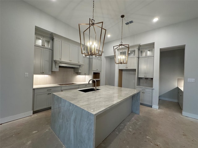 kitchen featuring sink, stovetop, a chandelier, decorative light fixtures, and a kitchen island with sink