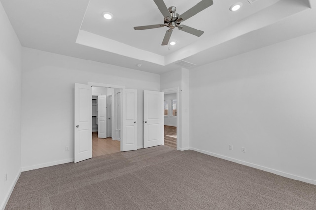 unfurnished bedroom with ceiling fan, a raised ceiling, and light colored carpet