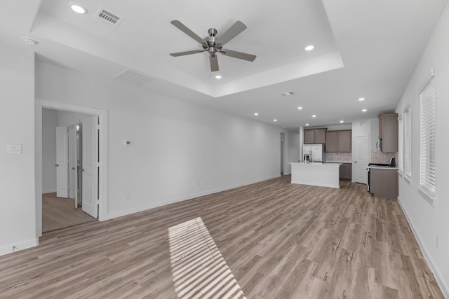 unfurnished living room featuring light wood-type flooring, a raised ceiling, and ceiling fan