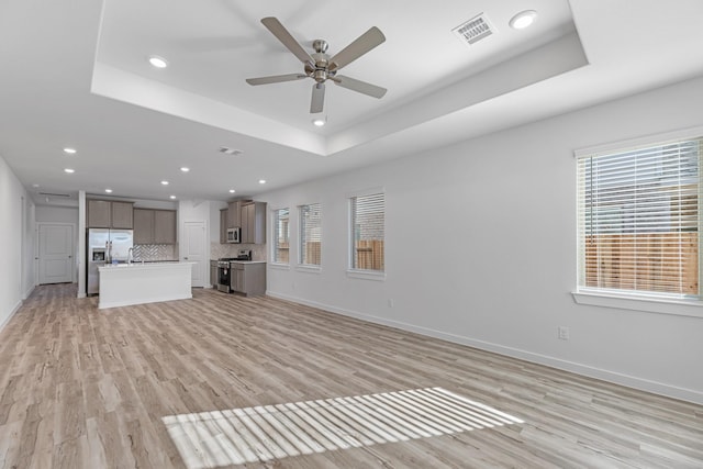 unfurnished living room featuring a raised ceiling, ceiling fan, and light hardwood / wood-style flooring