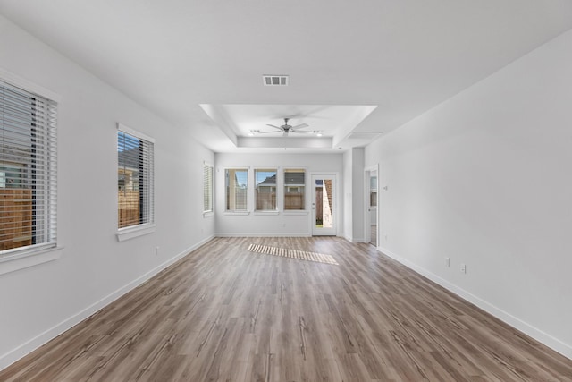 unfurnished living room with light hardwood / wood-style floors, a raised ceiling, and ceiling fan