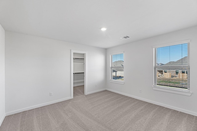 unfurnished bedroom with light colored carpet, a spacious closet, and a closet