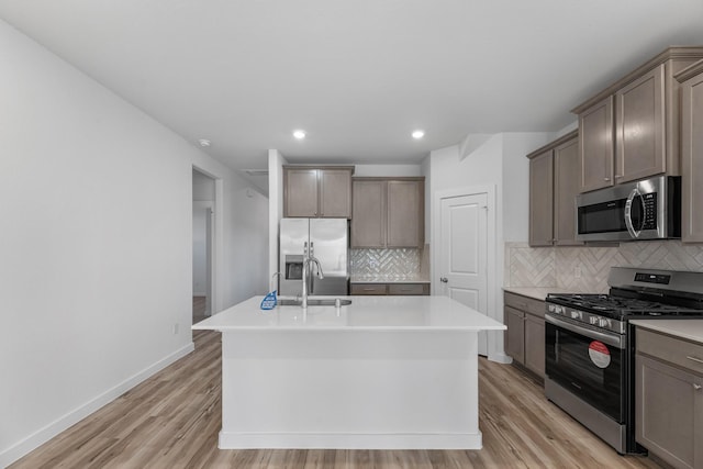 kitchen with sink, stainless steel appliances, light hardwood / wood-style flooring, decorative backsplash, and a center island with sink