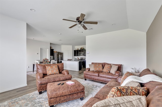 living room featuring vaulted ceiling, light hardwood / wood-style flooring, and ceiling fan