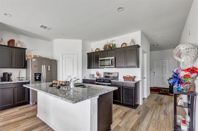 kitchen with an island with sink, light stone countertops, sink, light hardwood / wood-style floors, and appliances with stainless steel finishes