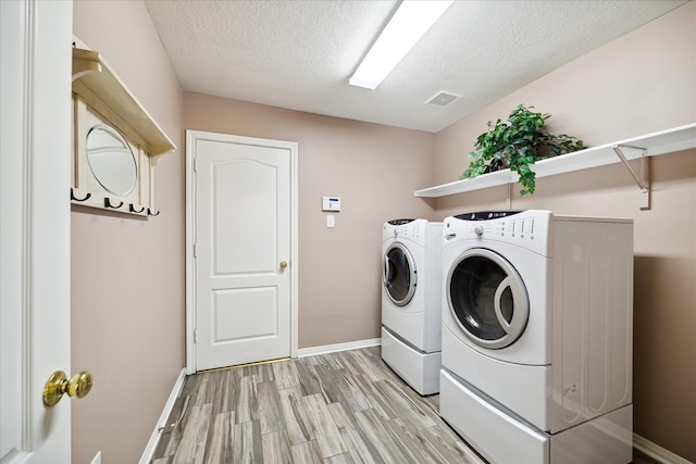 laundry room with washer and dryer, a textured ceiling, and light hardwood / wood-style flooring