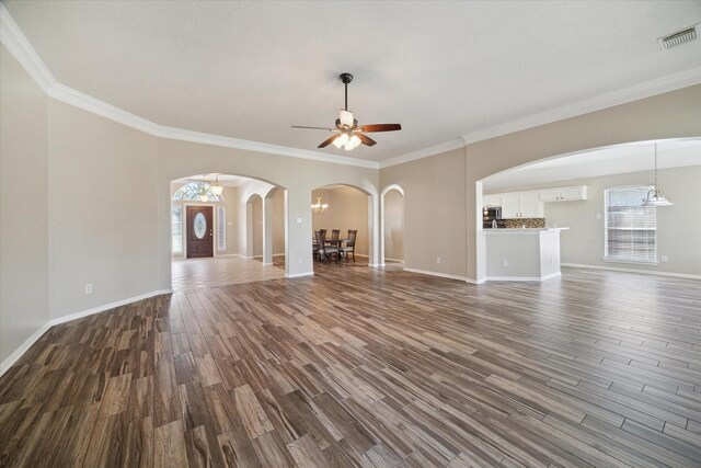 unfurnished living room featuring ornamental molding, ceiling fan with notable chandelier, and plenty of natural light