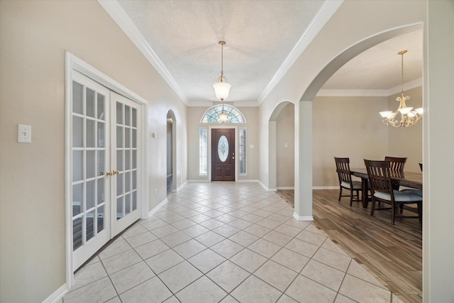 tiled entryway featuring french doors, ornamental molding, a notable chandelier, and a textured ceiling