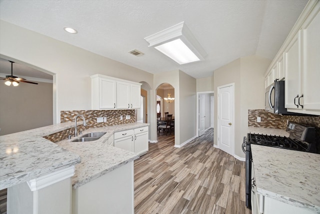 kitchen with black range with gas stovetop, kitchen peninsula, decorative backsplash, sink, and white cabinetry