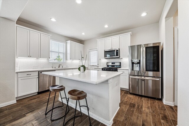 kitchen with appliances with stainless steel finishes, dark wood-type flooring, white cabinetry, and a center island