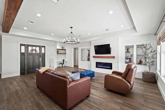 living room featuring a raised ceiling, dark hardwood / wood-style flooring, a fireplace, and a notable chandelier