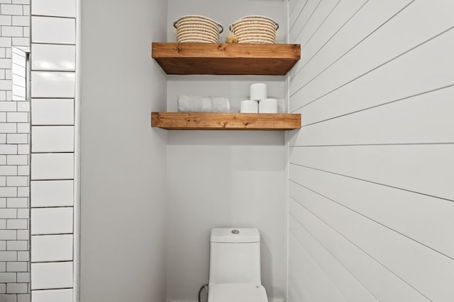 bathroom featuring wooden walls and toilet