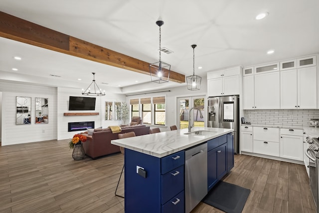 kitchen featuring white cabinetry, blue cabinets, an island with sink, and appliances with stainless steel finishes