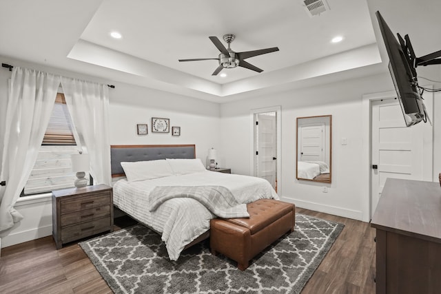 bedroom featuring ceiling fan, dark hardwood / wood-style flooring, and a tray ceiling