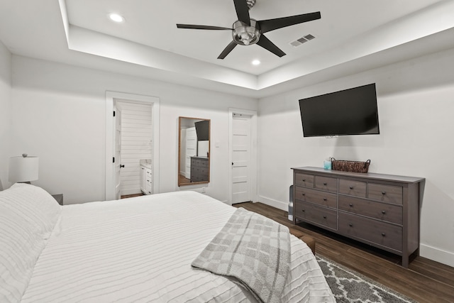 bedroom featuring a tray ceiling, ensuite bath, ceiling fan, and dark wood-type flooring