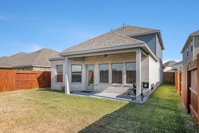 back of house featuring roof with shingles, a yard, brick siding, and a fenced backyard