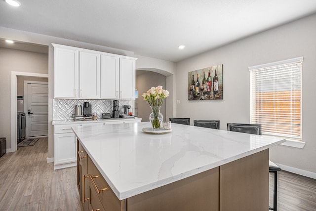 kitchen with light wood-type flooring, light stone countertops, backsplash, white cabinets, and a center island