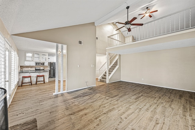 unfurnished living room with light hardwood / wood-style floors, high vaulted ceiling, beamed ceiling, and a textured ceiling