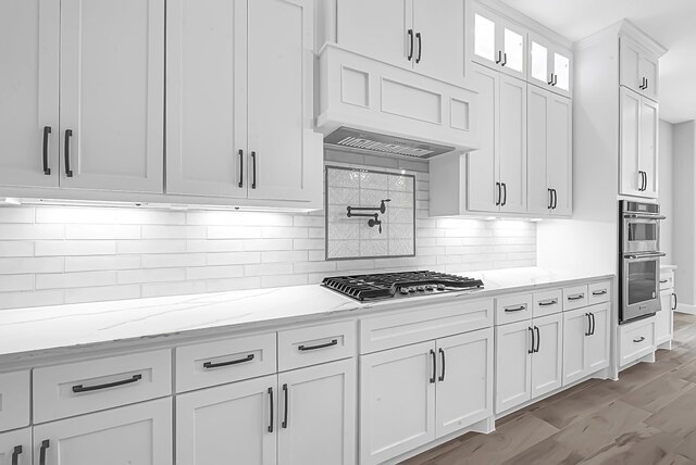 kitchen featuring light wood-type flooring, stainless steel appliances, light stone countertops, backsplash, and white cabinets