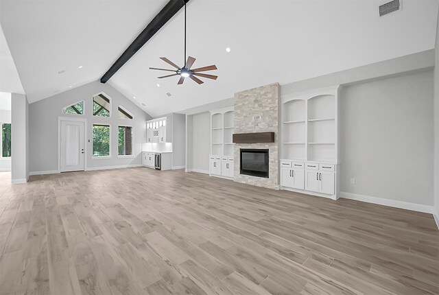 unfurnished living room featuring ceiling fan, beamed ceiling, light wood-type flooring, and a stone fireplace