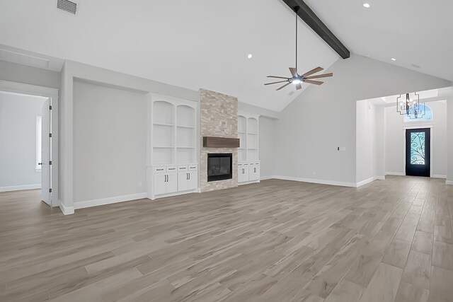 unfurnished living room with built in shelves, light wood-type flooring, ceiling fan with notable chandelier, beam ceiling, and a fireplace