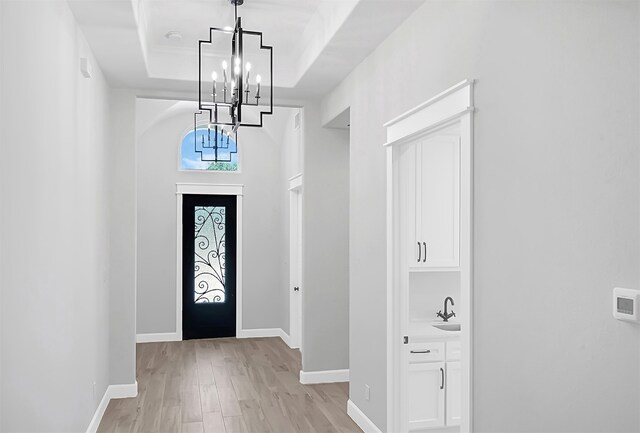 foyer entrance featuring light wood-type flooring, a tray ceiling, sink, and a chandelier