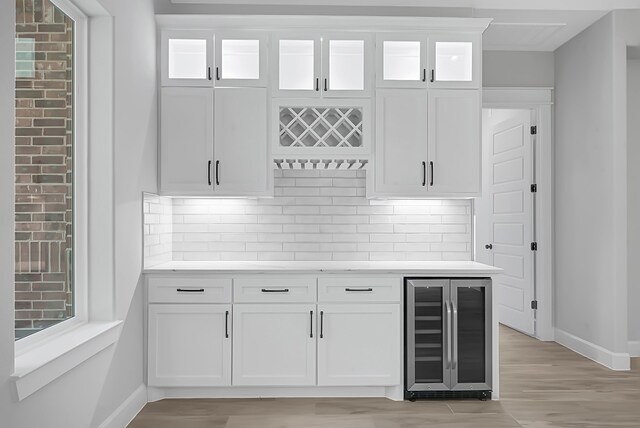 bar featuring tasteful backsplash, wine cooler, light wood-type flooring, and white cabinetry