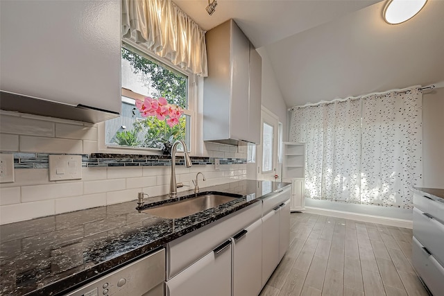 kitchen with dishwasher, white cabinetry, lofted ceiling, sink, and backsplash