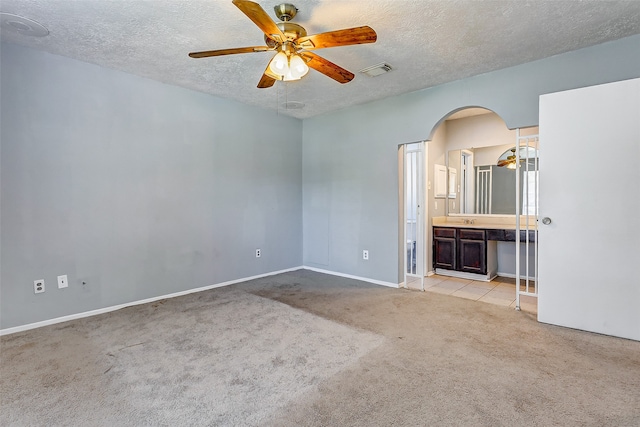 unfurnished bedroom featuring light colored carpet, ensuite bath, ceiling fan, and a textured ceiling