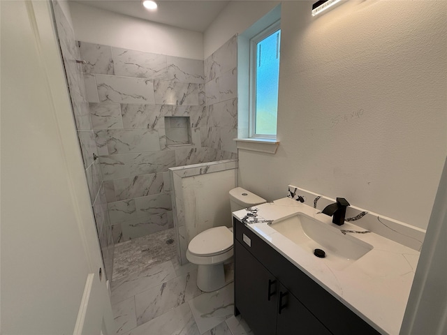 bathroom with a tile shower, toilet, and vanity