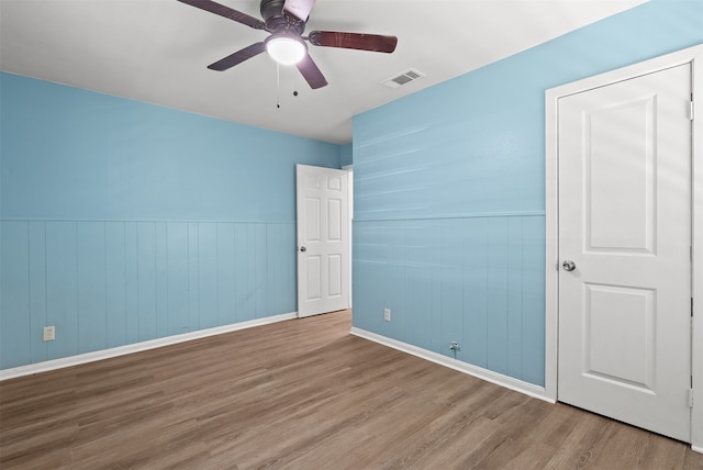 unfurnished bedroom featuring wooden walls, ceiling fan, and hardwood / wood-style floors