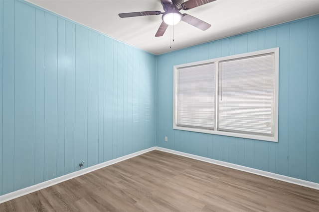 spare room with wood-type flooring, wooden walls, and ceiling fan