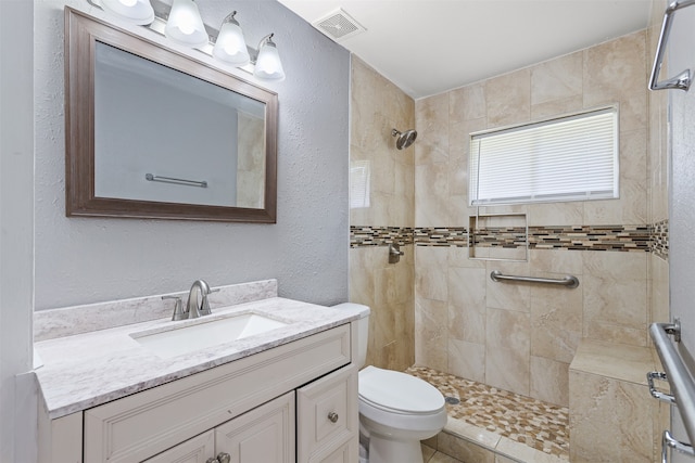 bathroom with a tile shower, tile patterned floors, vanity, and toilet