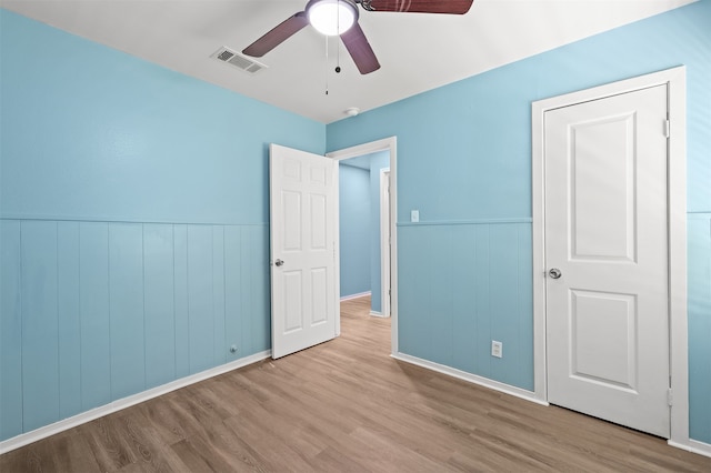 unfurnished bedroom featuring ceiling fan, wood walls, and light hardwood / wood-style flooring