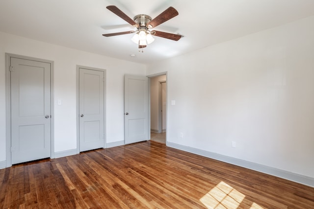 unfurnished bedroom with hardwood / wood-style floors, multiple closets, and ceiling fan