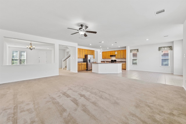 unfurnished living room featuring ceiling fan with notable chandelier and light colored carpet