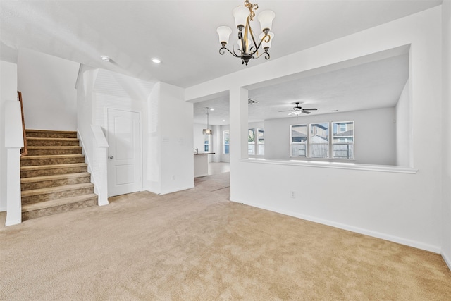 unfurnished living room featuring ceiling fan with notable chandelier and light carpet