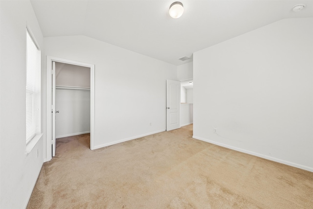 unfurnished bedroom with light carpet, a closet, vaulted ceiling, and a walk in closet