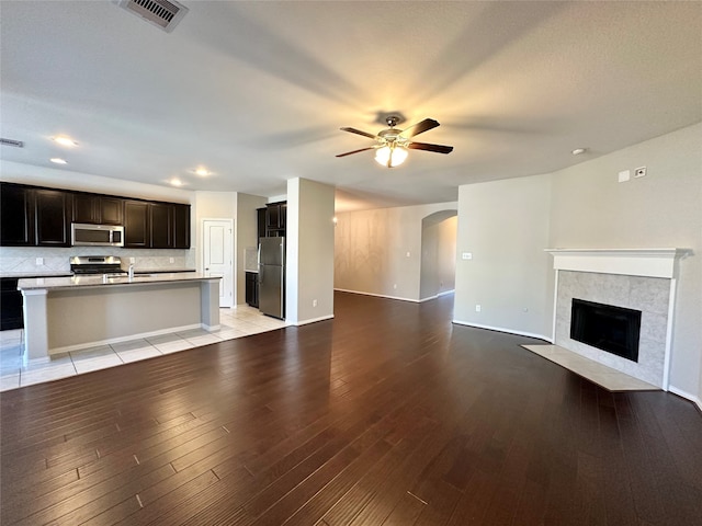 unfurnished living room featuring a fireplace, ceiling fan, sink, and light hardwood / wood-style flooring