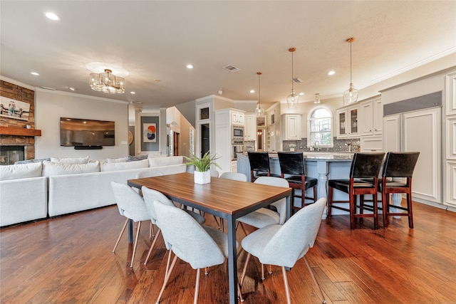 dining area featuring crown molding, dark hardwood / wood-style flooring, a notable chandelier, sink, and a stone fireplace