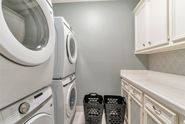 washroom featuring stacked washer / drying machine, light tile patterned floors, and cabinets