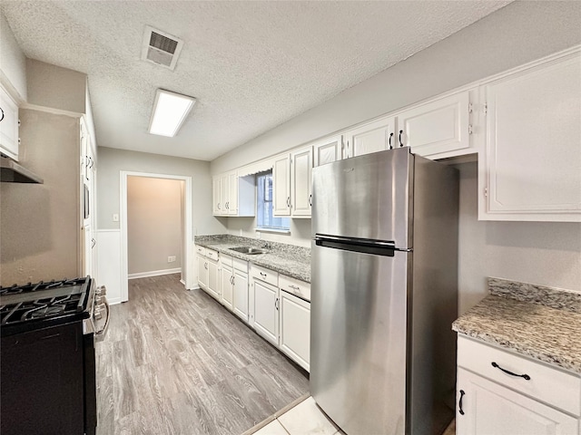 kitchen with light hardwood / wood-style floors, stainless steel refrigerator, white cabinets, and gas stove