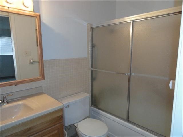 full bathroom featuring bath / shower combo with glass door, vanity, tile walls, and toilet