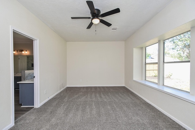 spare room with dark colored carpet, ceiling fan, and a textured ceiling