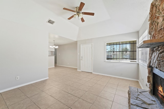 unfurnished living room featuring ceiling fan with notable chandelier, vaulted ceiling, a stone fireplace, and light tile patterned floors