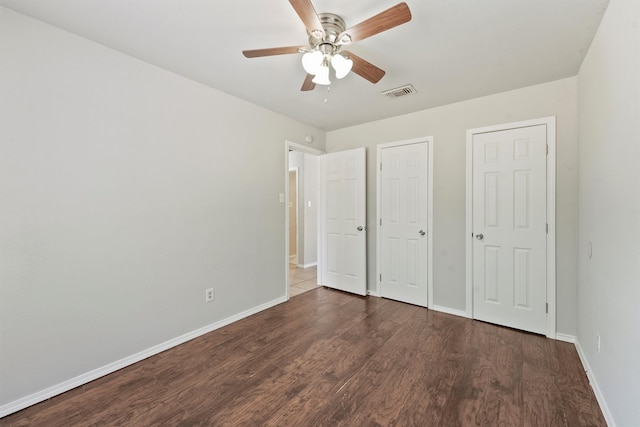 unfurnished bedroom featuring ceiling fan, two closets, and dark hardwood / wood-style floors