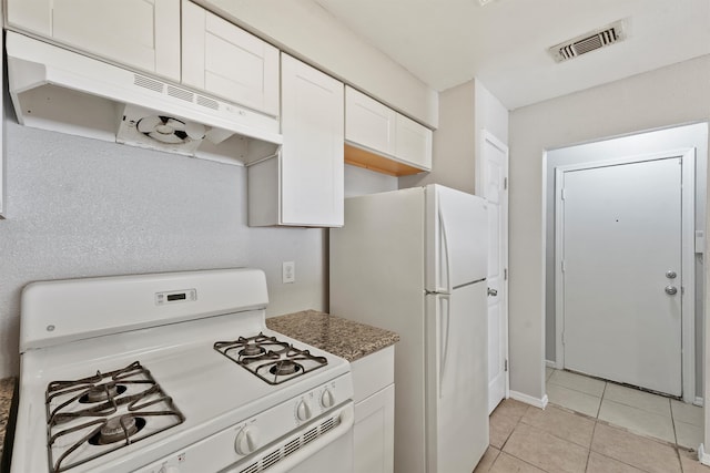 kitchen with dark stone countertops, light tile patterned flooring, white appliances, and white cabinetry