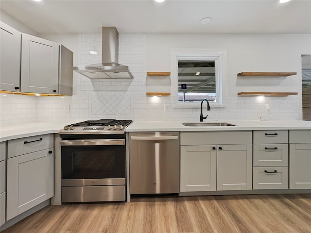 kitchen featuring tasteful backsplash, sink, wall chimney range hood, light hardwood / wood-style flooring, and appliances with stainless steel finishes